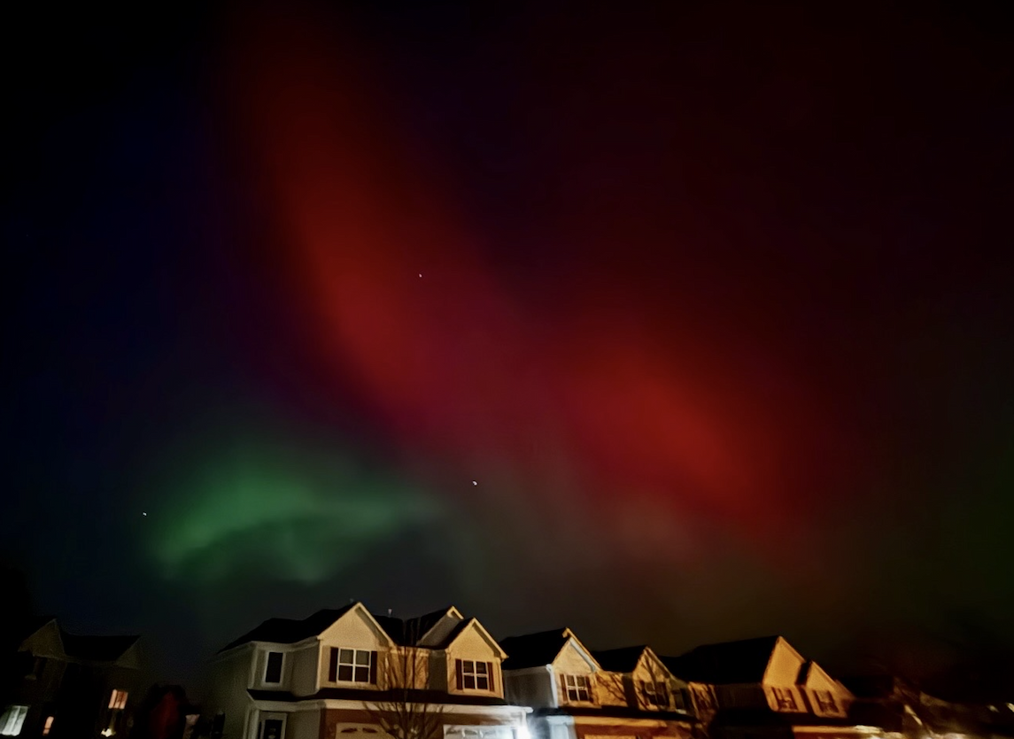 Red and green aurora lights over a row of homes