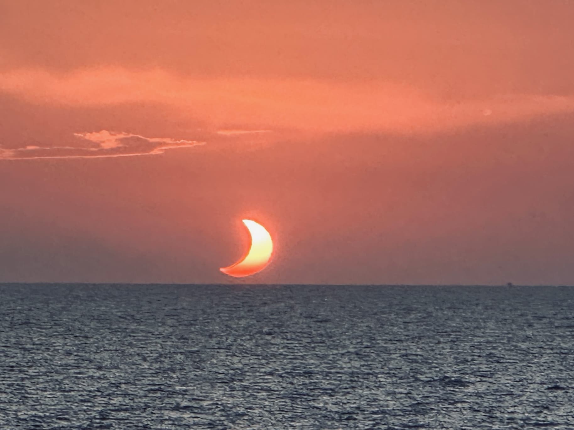 A partial solar eclipse of the sun as it hovers just above the ocean horizon