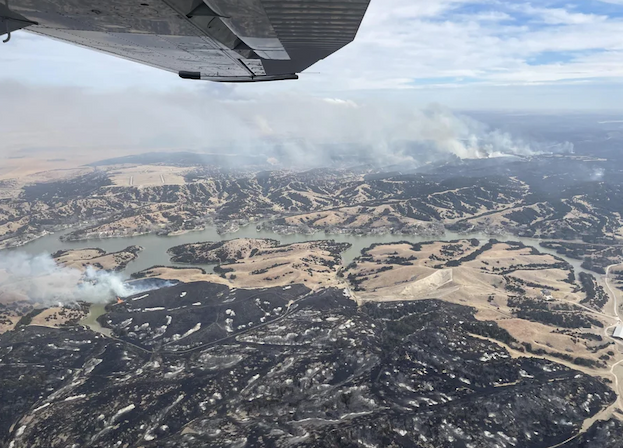A view from an airplane of smoke rising from arid lands.