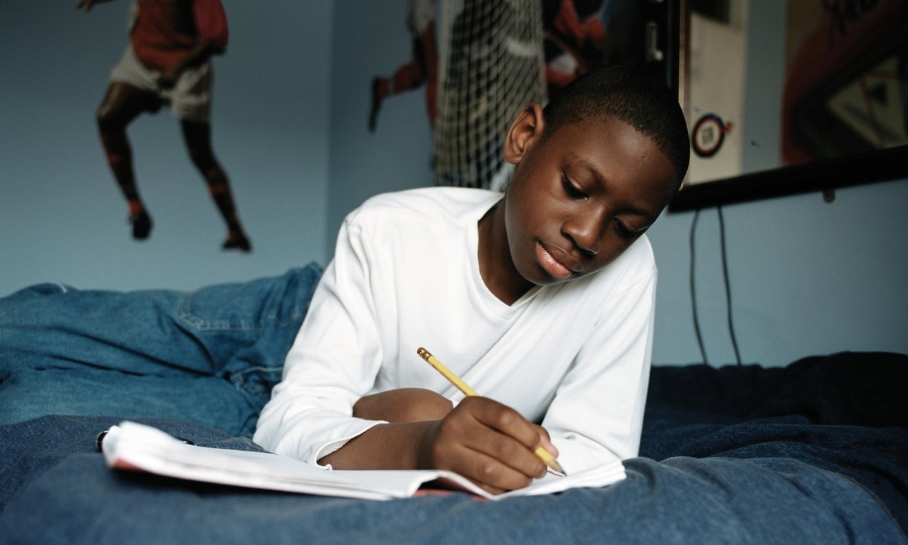Young person writing in notebook while lying on bed