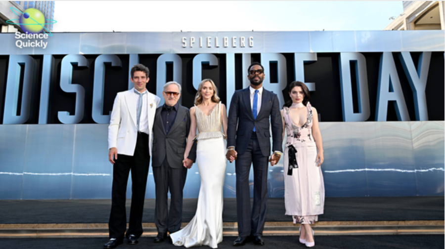 The director and cast of the movie Disclosure Day pose in front of a banner with the name of the movie for a promotional event