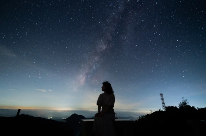 A silhouetted figure sitting on a bench beneath a dark starry sky