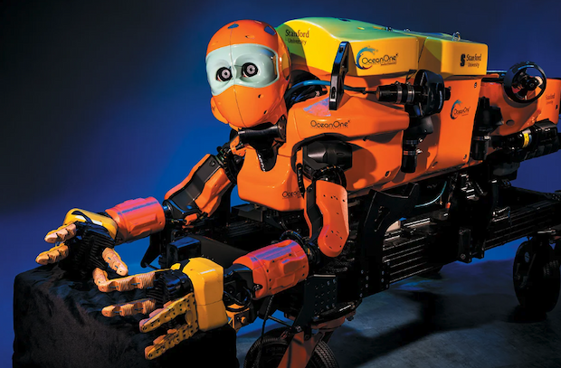 An orange, humanoid-looking robot with arms outstretched in front of it, mounted on a black wagon-type assembly.