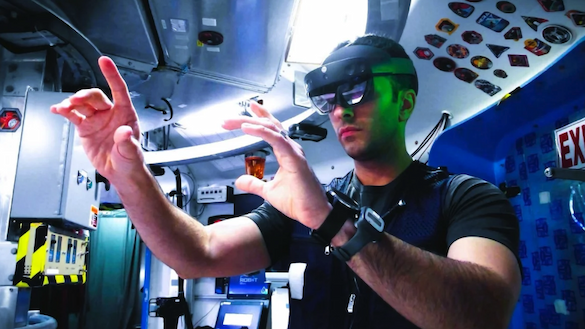 A man wears virtual reality goggles with his hands outstretched in a lab setting.