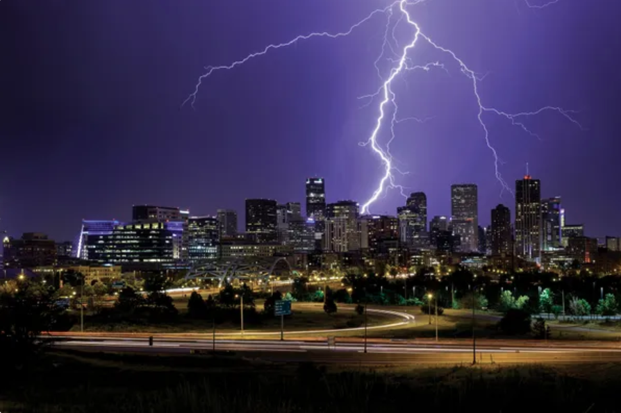 Bright lightning arcs through the night sky toward a city skyline.