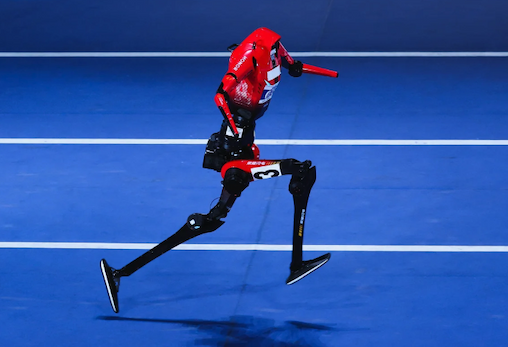 A red and black humanoid robot in mid-stride on a blue running track.