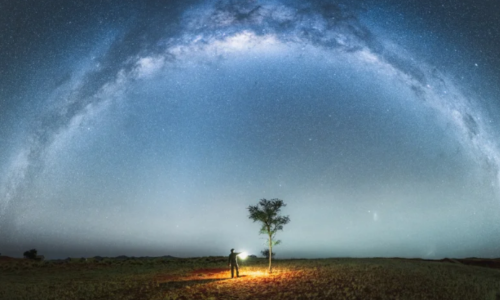 A panoramic landscape beneath a starry sky dominated by the arc of the Milky Way