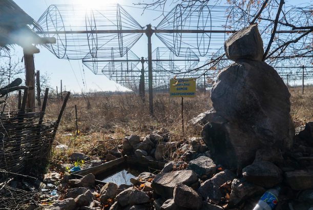 Boulders and trash are piled in the foreground of a large array of radio antennas beneath a sunny blue sky.