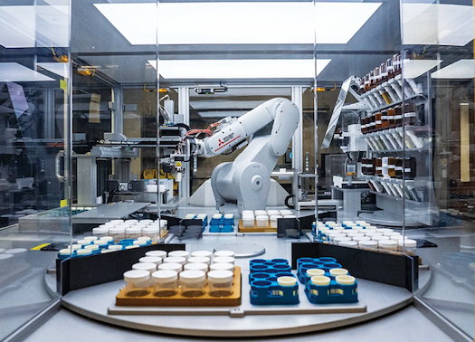 A robotic arm in a lab environment surrounded by sample cups