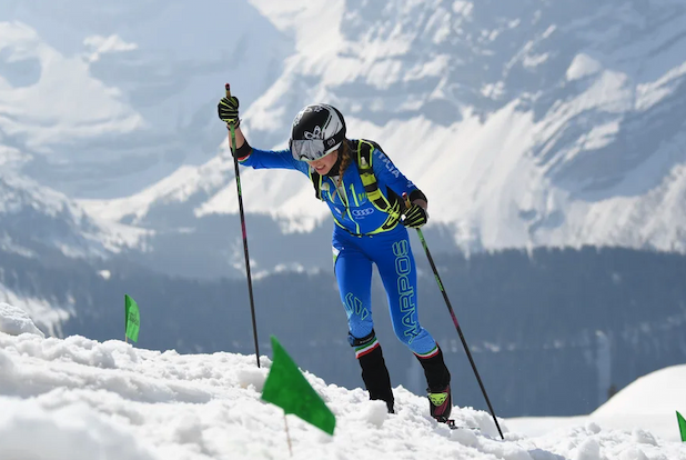 A ski mountaineer climbing a snowy hill and digging in her poles.