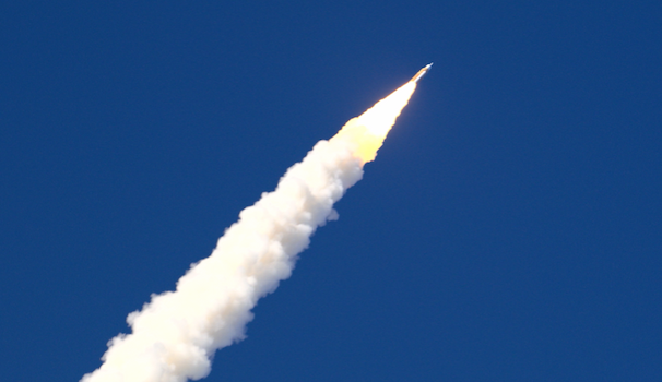 A rocket ship blasts to space against a deep blue sky