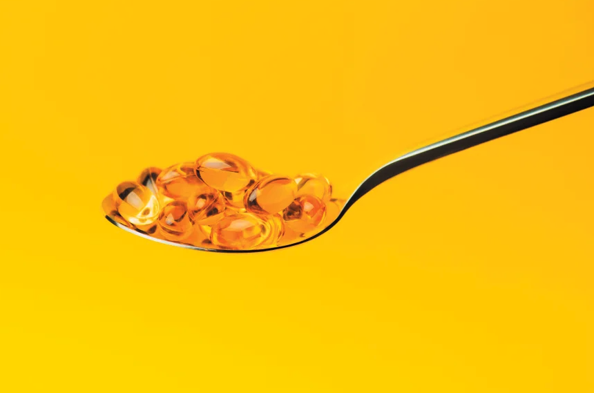 A spoon holds golden capsules, on a yellow background.