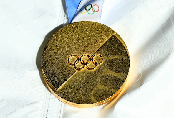 An Olympic gold medal with the six Olympic rings at its center and its ribbon emerging directly from the medal itself.