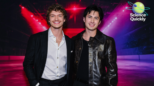 A color photo of Heated Rivalry actors Connor Storrie and Hudson Williams smiling and standing side by side.