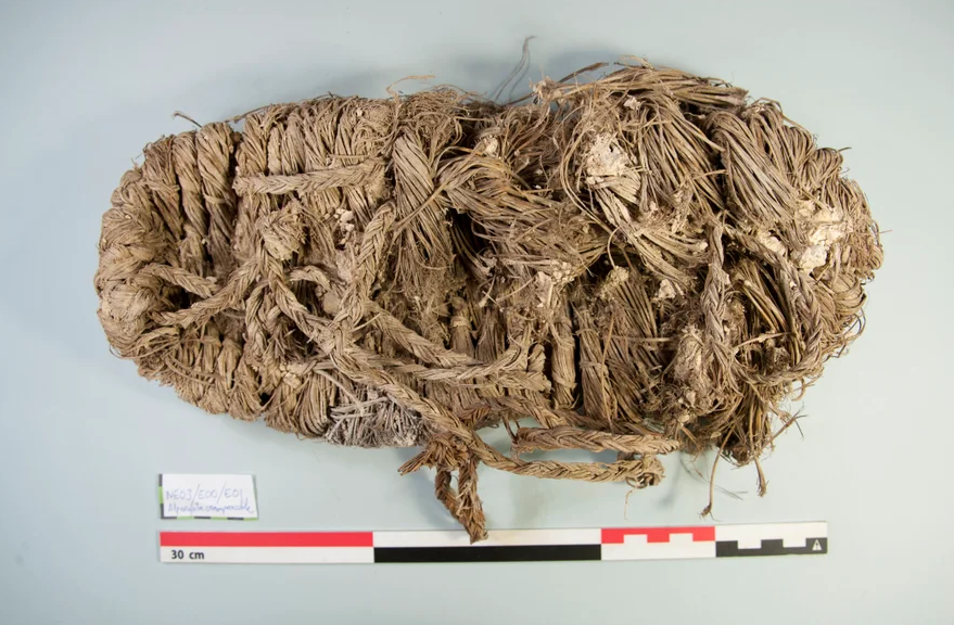 A woven grass shoe on a blank background near a 30 centimeter measuring stick.
