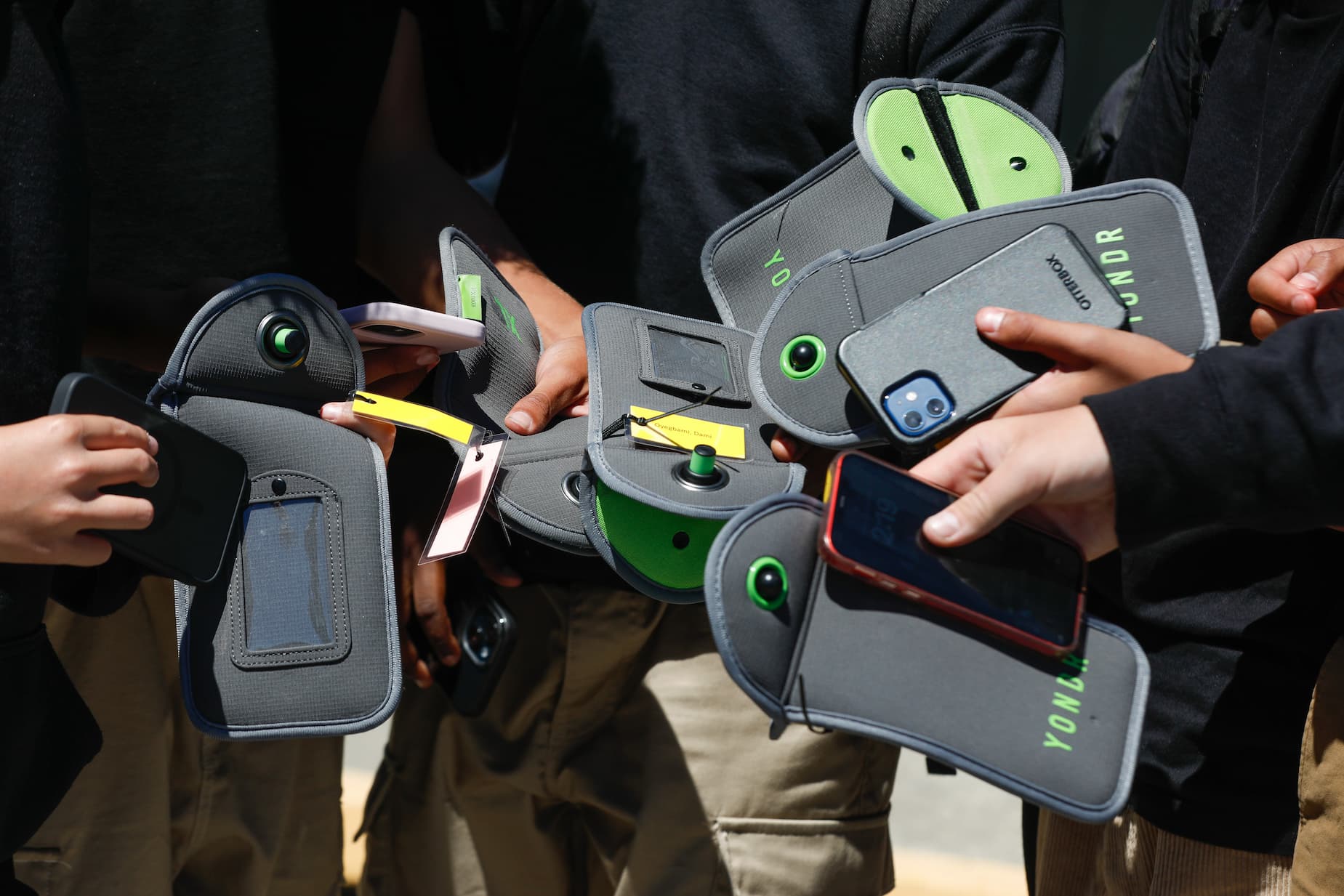 Kids' hands hold cell phones and pouches for storing them while in school