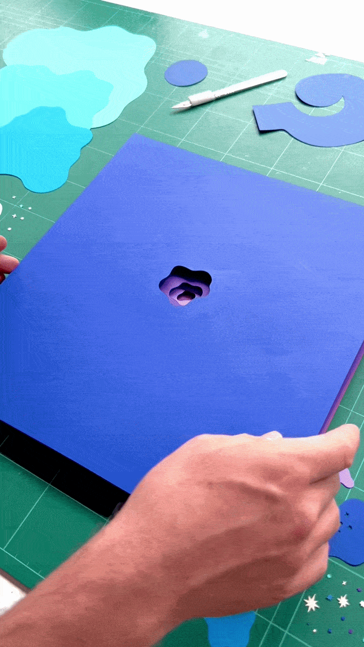 GIF of someone layering purple and blue pieces of paper, each with a swirly cutout.