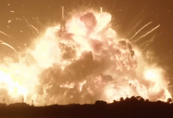 A firey explosion over dark trees in the foreground.