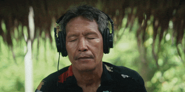 A GIF of an excerpt of a short documentary showing construction vehicles in a jungle setting, busy roads and bustling city life, interspersed with scenes of a man listening to headphones in the forest.