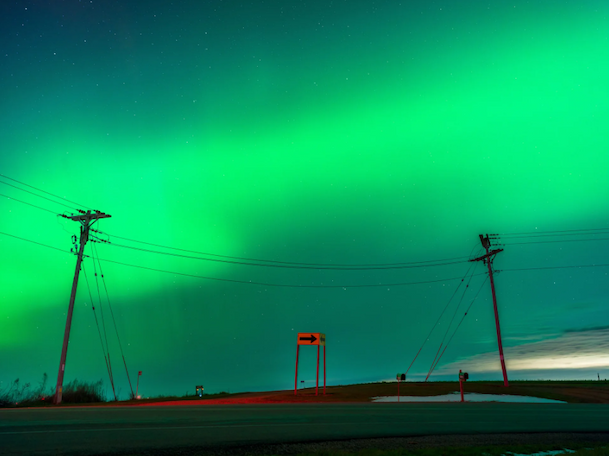 Bright green auroras across the central part of the sky with power lines in the foreground