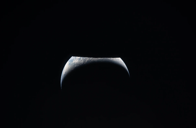 A crescent of Earth below the darkness of the moon's outline