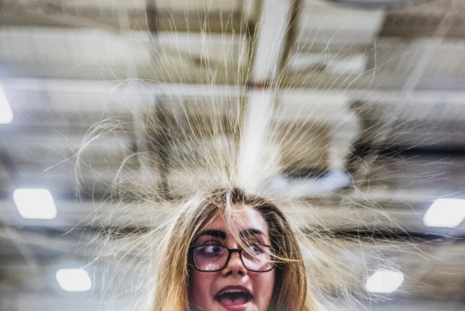 A woman with glasses looks off camera with surprise as her blond hair stands on end