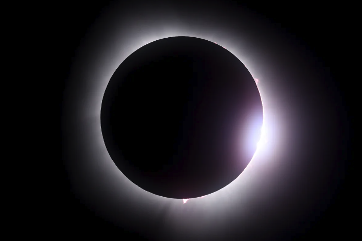 The moon in front of the sun during an eclipse. Solar flares in the sun's corona are visible.