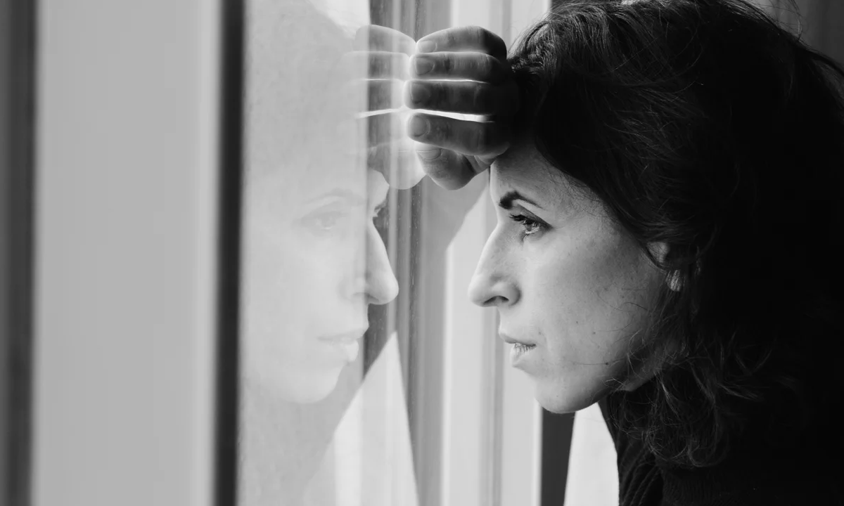 Black and white image of lady solemnly gazing out window