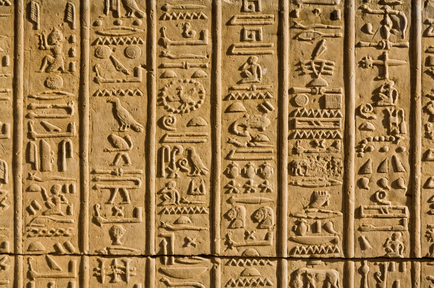 Alt text: Close-up of ancient Egyptian hieroglyphs carved in vertical columns on a tan stone wall.