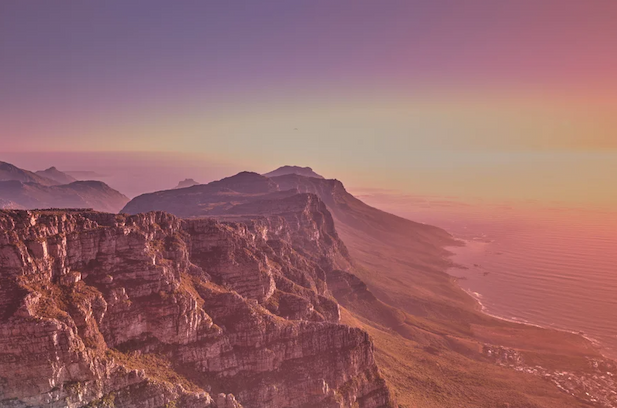 Mountain and ocean landscape with pinks and orange hues.