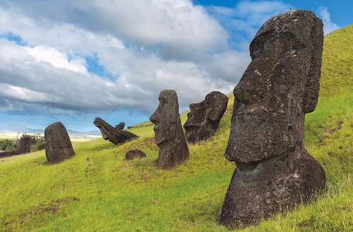 Moai statues, some upright, some leaning, on a grassy hillside. 