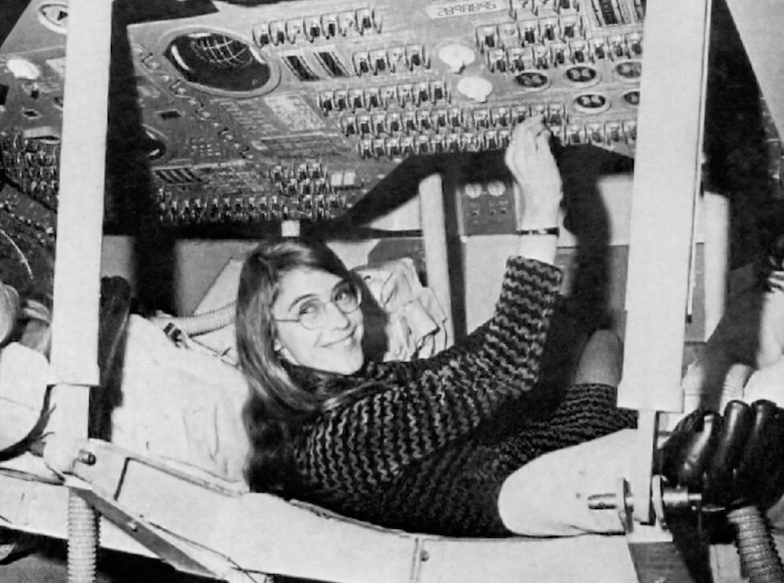 A woman in glasses sitting inside a spacecraft in black and white.