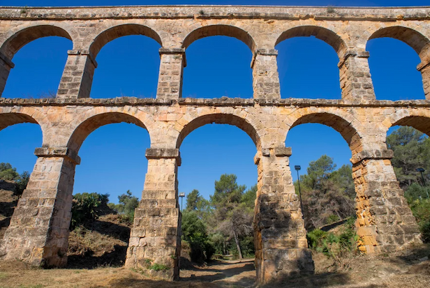 A double set of stone arches set against a blue sky and muted green trees