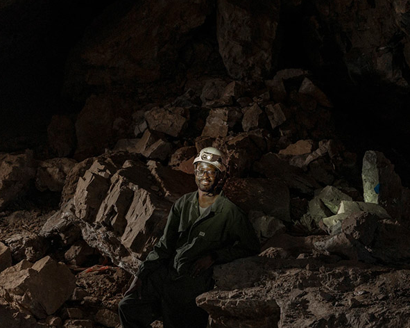 A man sitting in a dark cave wearing a helmet