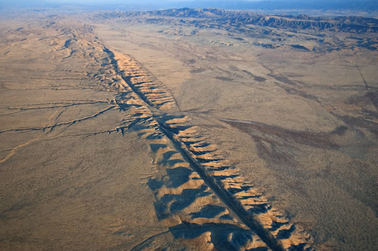 An aerial view of a geologic fault line showing buckled land lining a large crevasse in the Earth