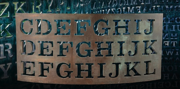 A copper plate with letters cut out of it in front of the Kryptos puzzle