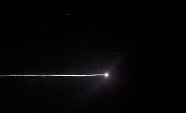 A beam of light moves across the black sky, from left to right.