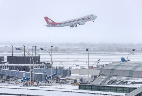 A plane takes off from a snowy runway with jet bridges and other airport infrastructure in the foreground