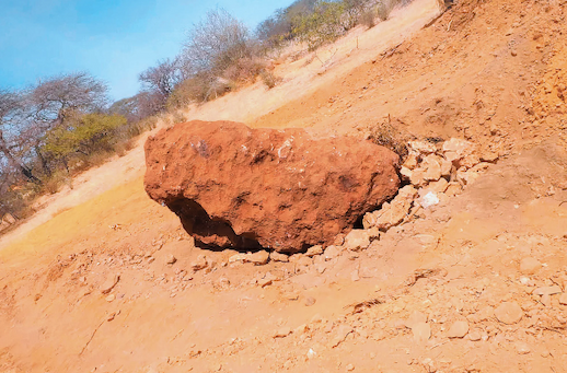 A large puckered red rock sits in an arid, sandy environment.