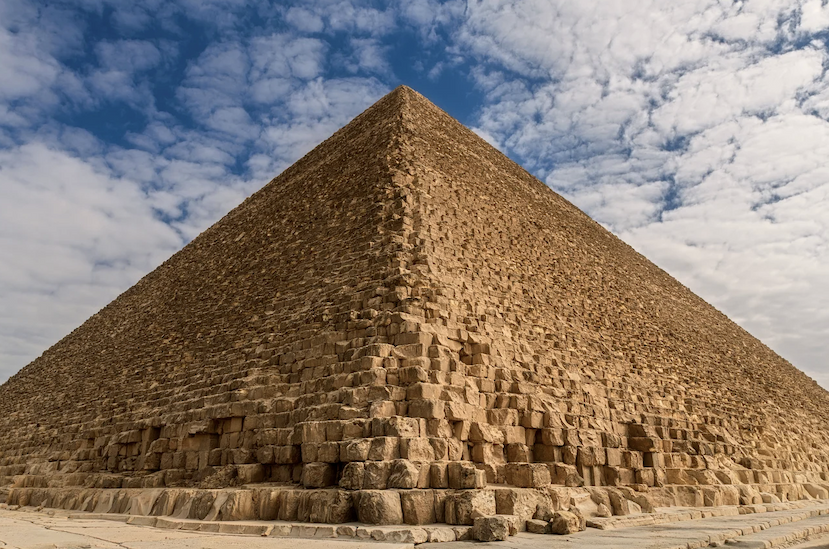 A head-on photograph of the Great Pyramid with a blue sky and cirrus clouds behind.