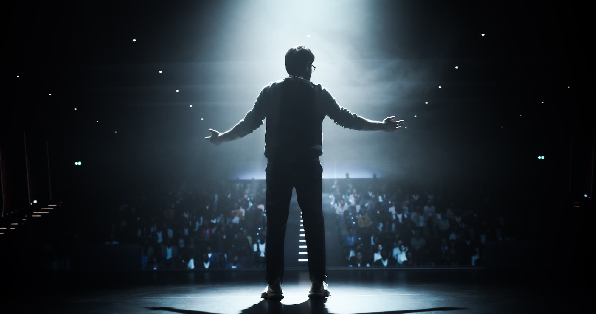 Silhouette of a man on stage in front of a crowd with his arms outstretched