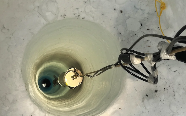 A metallic device is lowered down a bored-out hole in ice.