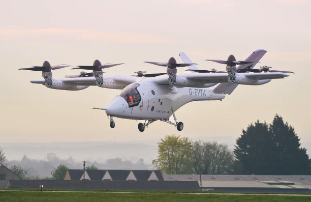 A helicopter-looking craft with eight vertical propellers hovers above an airfield.