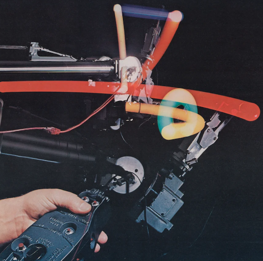 A multiple-exposure photo showing a person holding a control device connected to a robot. Overlaid photographs showed blurred action of a robot's gripper hand in different movements.