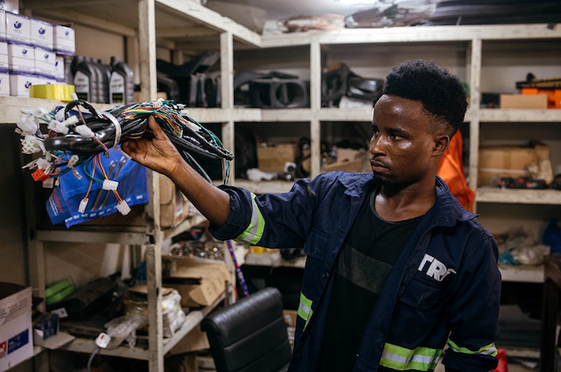 Erasto Job picks up a bundle of chargers from a shelf for electric bajajis at the Tri workshop in Dar es Salaam, Tanzania.