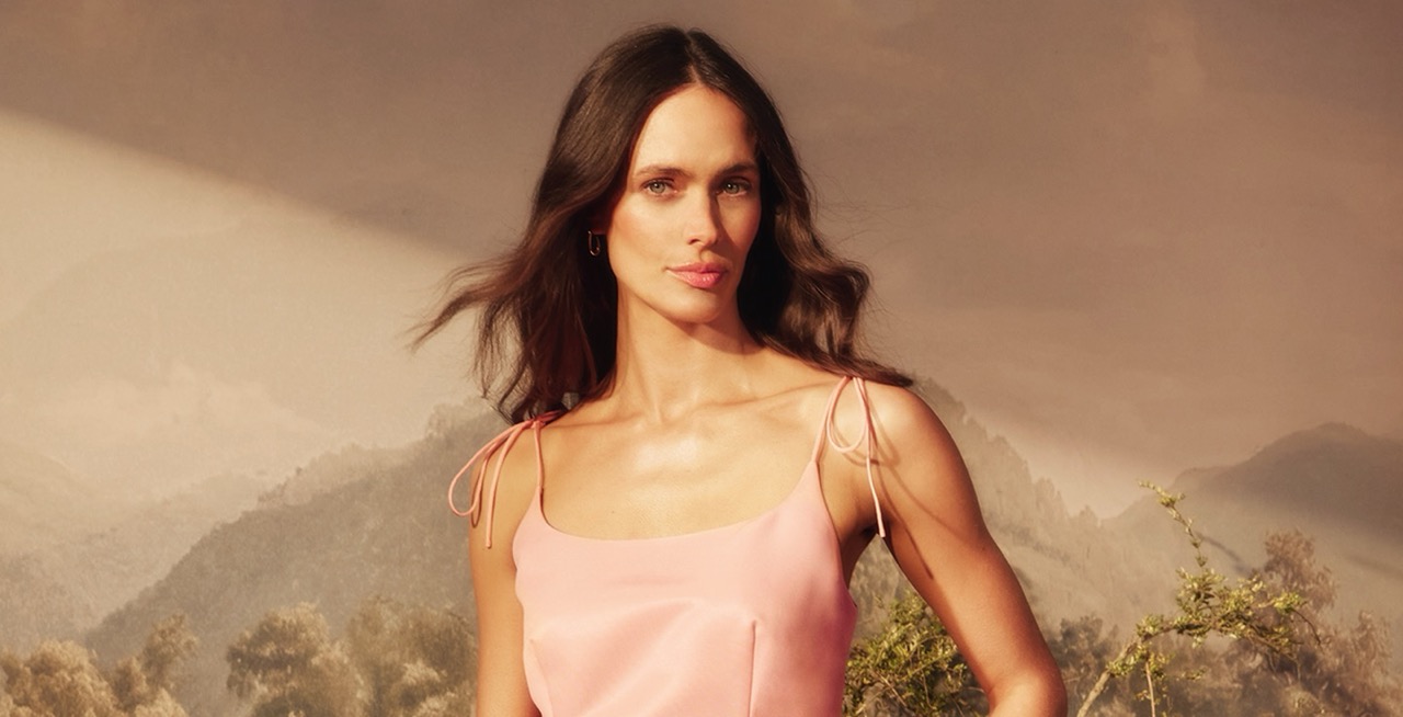 Woman in pink tie-strap dress against a mountain landscape backdrop