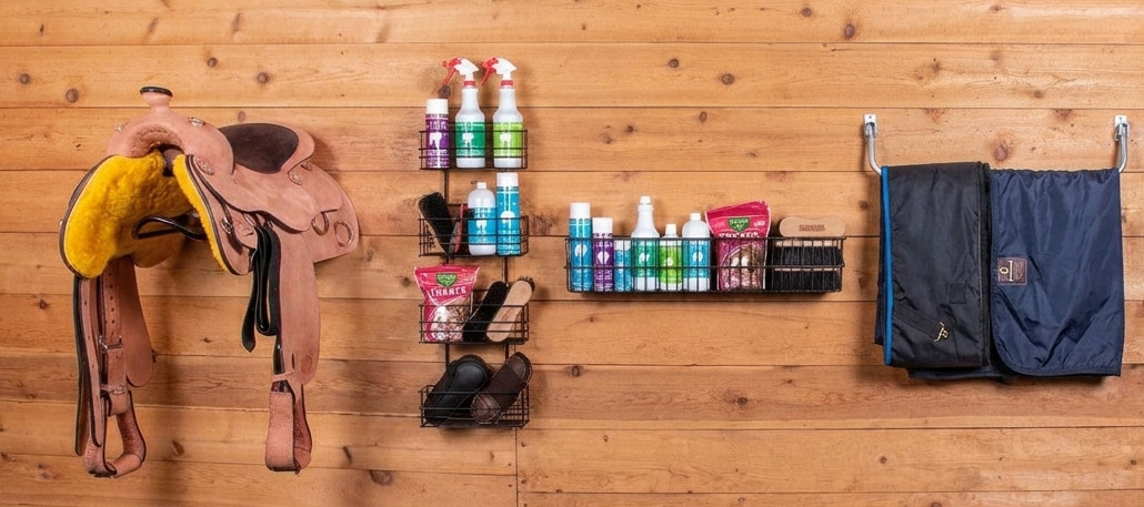 An organized tack room with saddle racks, grooming baskets, a bridle rack, and a blanket bar on a wood wall