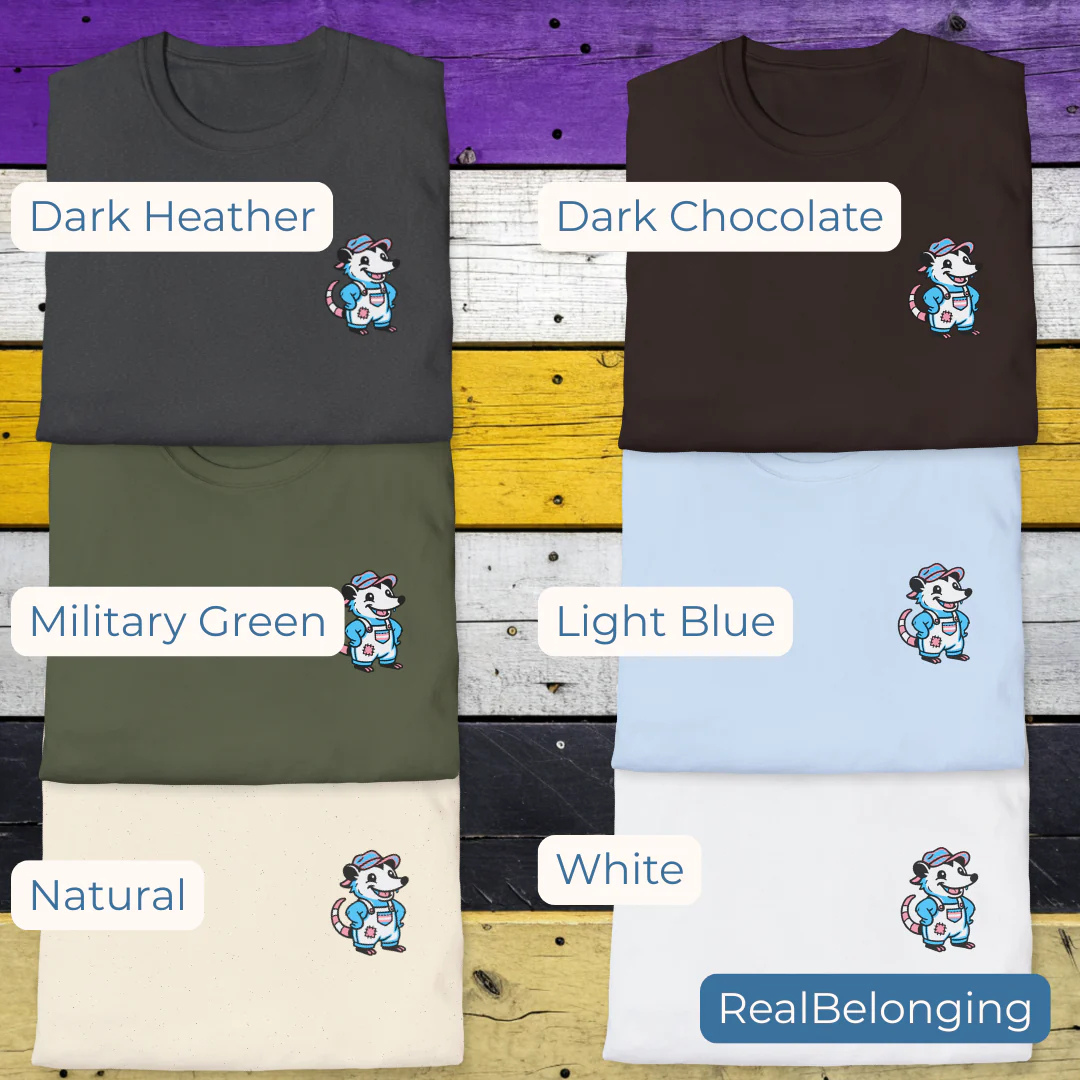 Flat-lay of six t-shirts with a 4" transgender opossum in overalls design on the chest