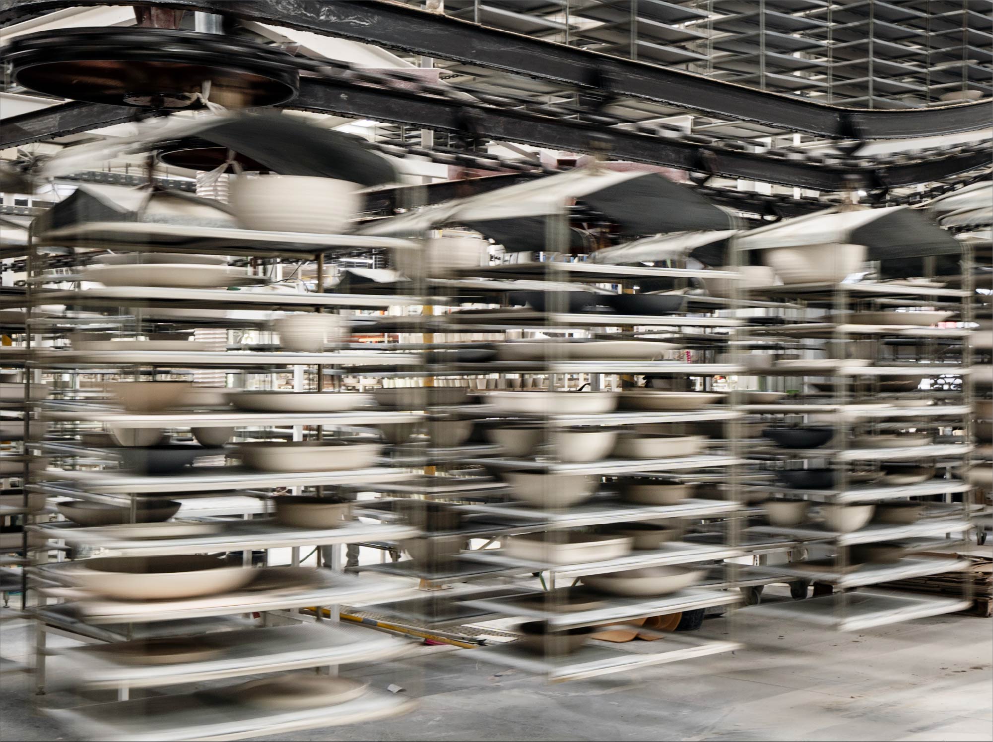Learn More button above a photograph of industrial shelves with stoneware pieces drying, shown in motion effect