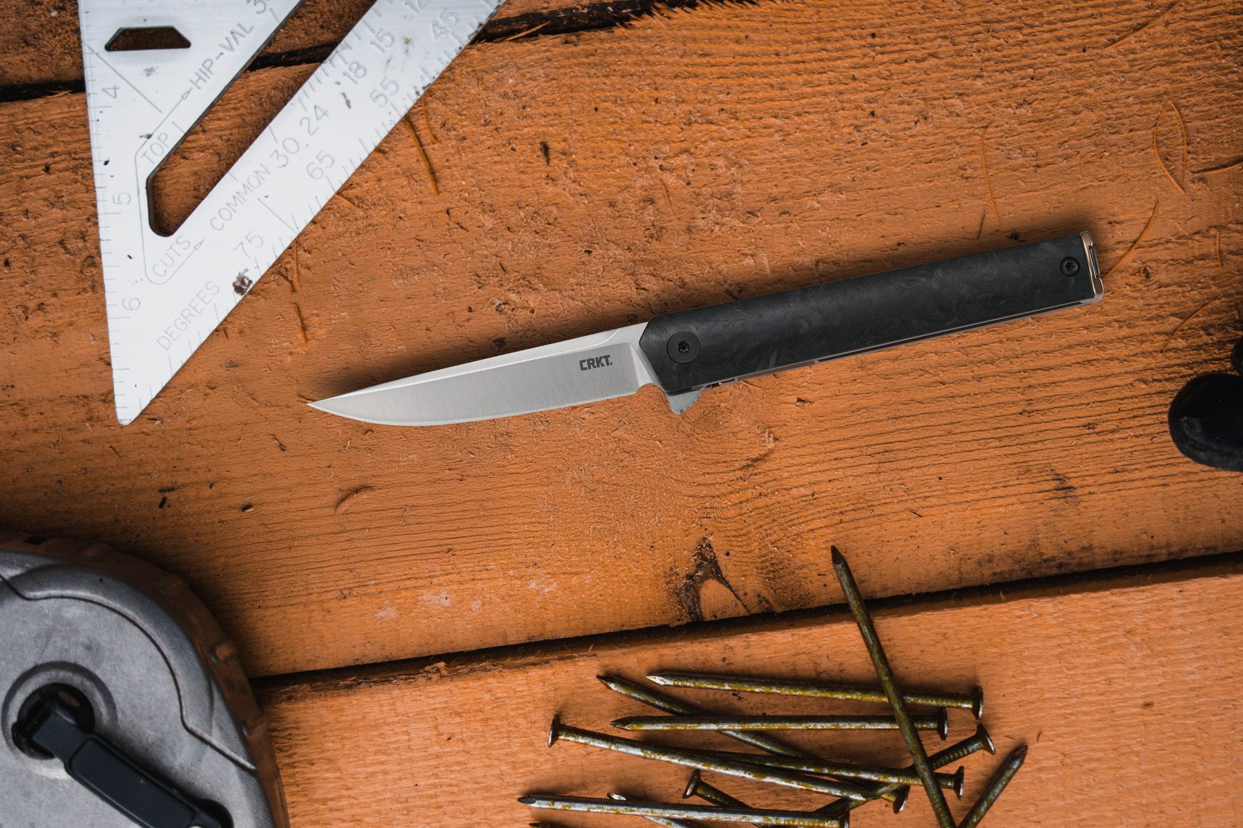 CEO Compact folding knife displayed on a woodworking bench alongside tools and nails.